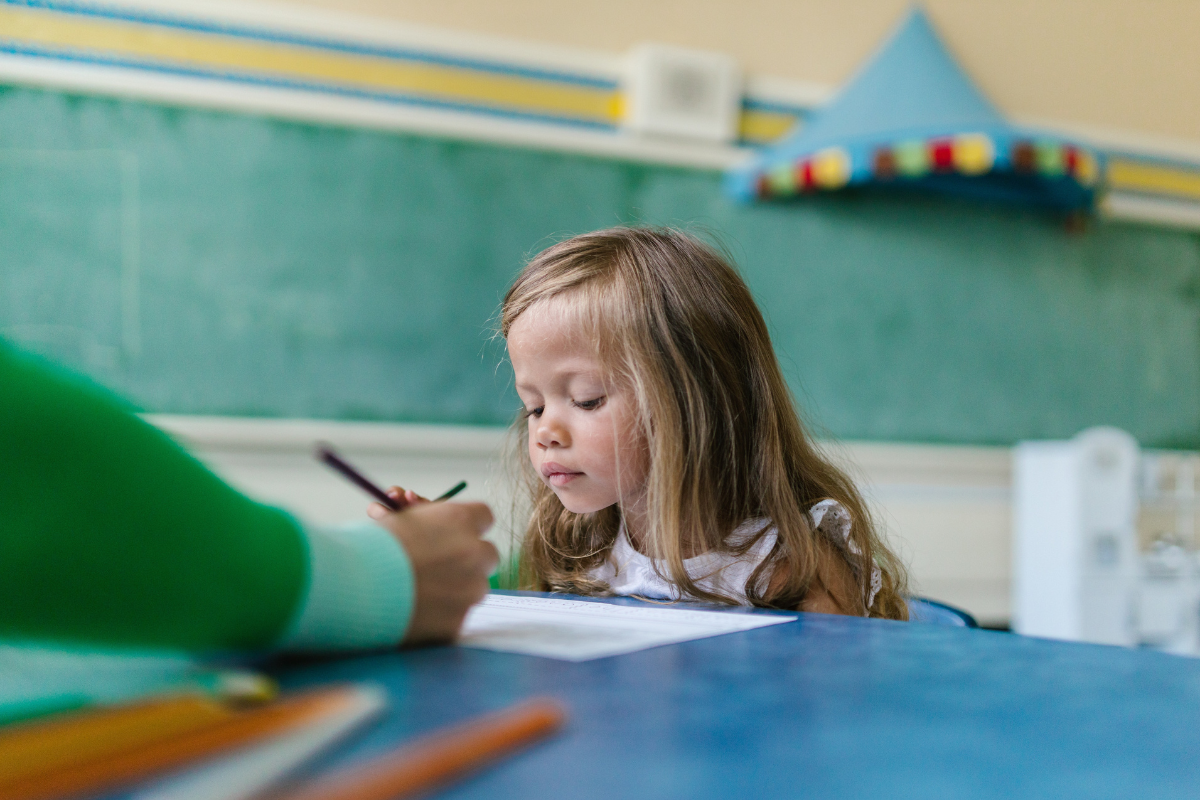 Foto de una niña leyendo algo que le señala la mano de la profesora